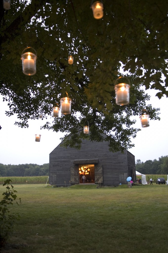 mason jar lights hanging from tree with barn wedding in background